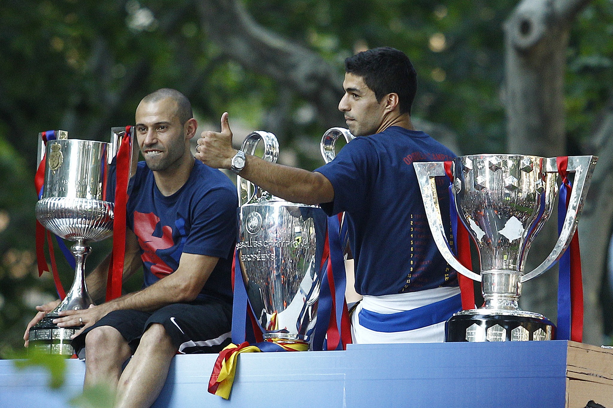 Barcelona's Uruguayan forward Luis Suarez (R) and Barcelona's Argentinian defender Javier Mascherano pose with the three trophies on a bus parading through the streets of Barcelona as the team celebrate its victory over Juventus one day after the UEFA Champions League final football on June 7, 2015. Luis Suarez and Neymar scored second-half goals to give Barcelona a 3-1 Champions League final victory over Juventus on June 6, 2015 as the Spaniards became the first team to twice win the European treble. AFP PHOTO/ QUIQUE GARCIA (Photo credit should read QUIQUE GARCIA/AFP/Getty Images)
